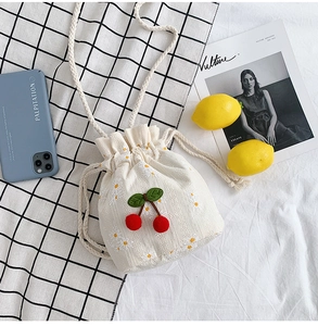 Detail of canvas bucket bag featuring daisy embroidery and 3D plush cherry charms