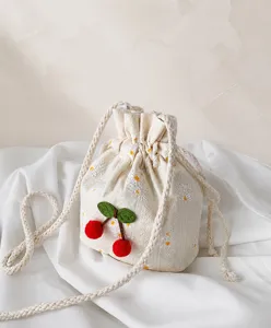 Détail du sac seau en toile crème avec pompons cerise et broderies de fleurs blanches