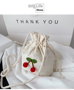Close-up of cream canvas bucket bag with cherry pom-poms and floral embroidery details