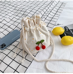 Detailed close-up of cream canvas bucket bag with daisy embroidery and plush cherry decor