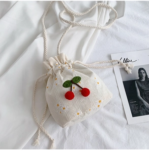 Close-up of white canvas drawstring bag with cherry and daisy embroidery and woven strap