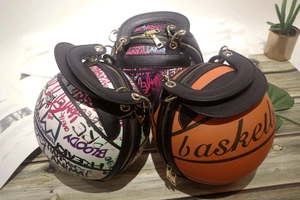 Three creative basketball-shaped purses in orange, white, and black graffiti on a desk