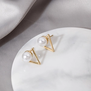 Elegant gold triangle metal stud earrings with white pearls on a marble display