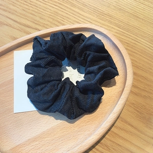 Detail of black corduroy scrunchie showing striped texture on a wooden background
