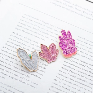 Tre spille in smalto a grappolo di cristallo colorato con glitter su sfondo libro