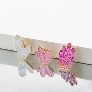 Dettaglio di tre spille in smalto a forma di cristallo glitterato con cornice dorata