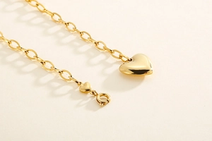 Close-up of polished gold heart pendant with a delicate link chain on beige background