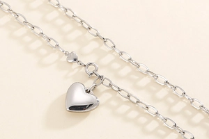 Macro shot of silver stainless steel necklace with 3D heart pendant on beige background