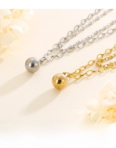 Macro shot of gold and silver bean pendant double chain necklaces on warm beige surface