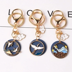 Detail of three blue enamel keychains with crane and wave patterns on white background
