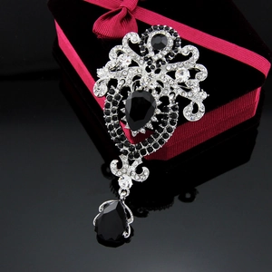 Detailed view of a vintage silver crown brooch with crystals on a black reflective surface
