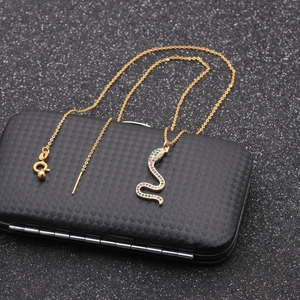 Close-up of a gold snake pendant with multi-color stones on a textured black box