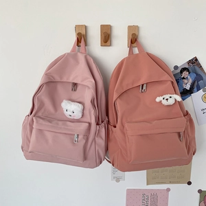 Dettagli di zaini in nylon rosa con graziosi ciondoli di peluche appesi ai ganci