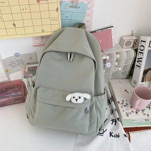 Dettaglio dello zaino in nylon verde impermeabile con ciondolo a forma di cucciolo bianco
