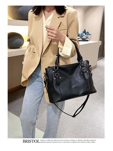 Detail of black pebbled leather tote bag with decorative straps and top handles for women