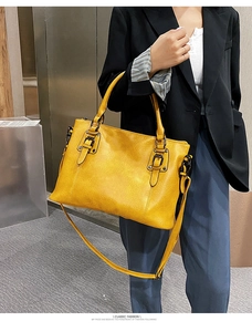 Detailed view of yellow faux leather tote bag with dual buckle straps and textured finish