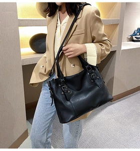 Black leather tote bag with metal buckle detail and shoulder strap on model display