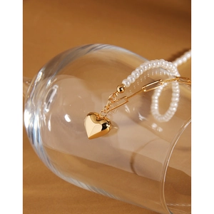 Detail of gold heart pendant and pearl chain draped over a clear glass on warm background