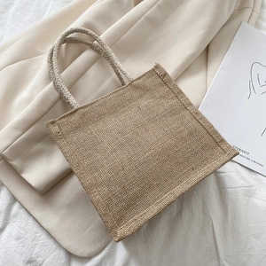 Minimalist jute tote bag with braided handles on soft fabric backdrop, large capacity