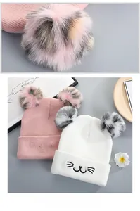 Detail of cute cat embroidery and large faux fur pom-poms on soft knitted beanies