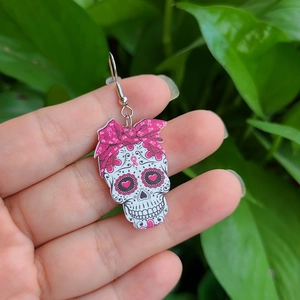 Detail der Acryl-Totenkopf-Ohrringe mit rosa Schleifen-Blumenmuster auf Naturhintergrund