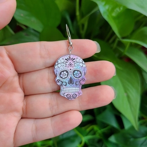 Makroaufnahme von farbenfrohen Totenkopf-Ohrringen mit Blumen in der Hand gehalten