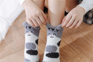 Close-up of cute grey and white plush coral fleece cat socks worn on wooden floor
