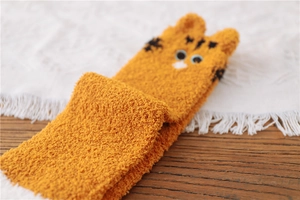 Detail of orange cat-themed coral fleece socks with 3D ears on a dark wooden background