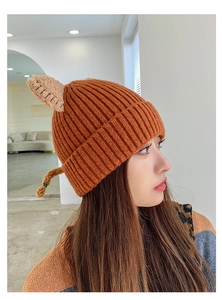 Close-up of caramel knit beanie featuring cute cat ears and braided tassel details