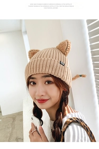 Close-up of beige knitted beanie with cat ear design and a black CAT brand label