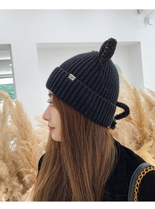 Detail shot of a black knitted beanie with cute cat ears and a small metal CAT logo