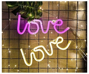 Pink and warm white LED neon love signs hanging on a wire mesh with fairy lights