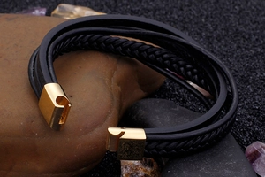 Detail of multi-layer black braided leather bracelet with a gold-tone alloy metal clasp