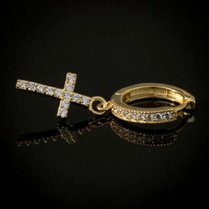 Detail of gold-plated hoop earring with crystal-encrusted cross pendant on black surface