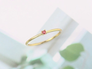 Close-up of minimalist gold ring with a single red gemstone in a four-prong setting