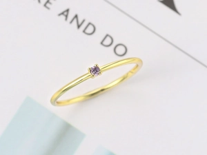 Macro shot of minimalist gold ring featuring a four-prong set round purple zircon crystal