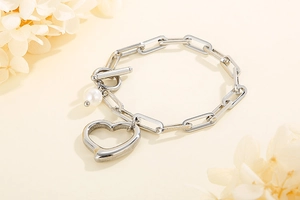 Detailed view of silver stainless steel chain bracelet with heart and pearl charms and T-bar clasp