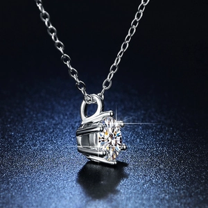 Macro view of six-prong solitaire moissanite pendant on a silver cross chain necklace