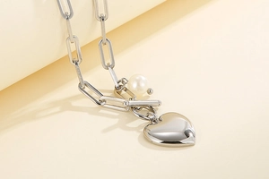 Détail d'un collier chaîne trombone argenté avec pendentif cœur et breloque perle blanche