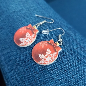 Close-up of red Christmas ball earrings with white snowflake patterns on blue fabric