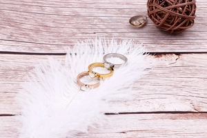 Three heart-shaped rings in gold, silver and rose gold finishes on white feathers