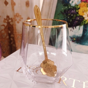 Detail of hexagon glass cup with gold rim and elegant flower-shaped golden metal spoon