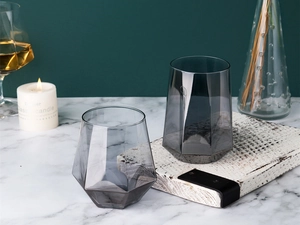 Detail of clear and smoky gray geometric faceted glass cups on a marble surface