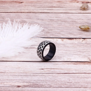 Detail of a two-tone punk rock ring with honeycomb cutout design on light wood surface