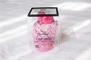 Close-up of pink coral fleece socks shaped like a cupcake in a clear gift box with pom-poms