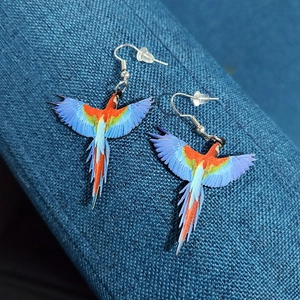 Close-up of laser-cut acrylic parrot earrings with vibrant blue and red feather details