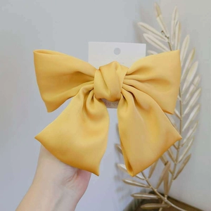 Detailed view of the bright yellow silk bow hair clip with smooth satin texture and metal grip