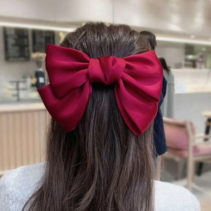 Detail of a large wine red silk bow hair clip worn on the back of the head on a model
