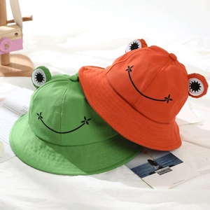 Detail shot of green and orange frog bucket hats with 3D eyes and embroidered smiles