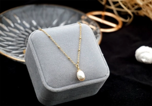 Macro shot of minimalist pearl pendant necklace on a premium grey velvet jewelry box